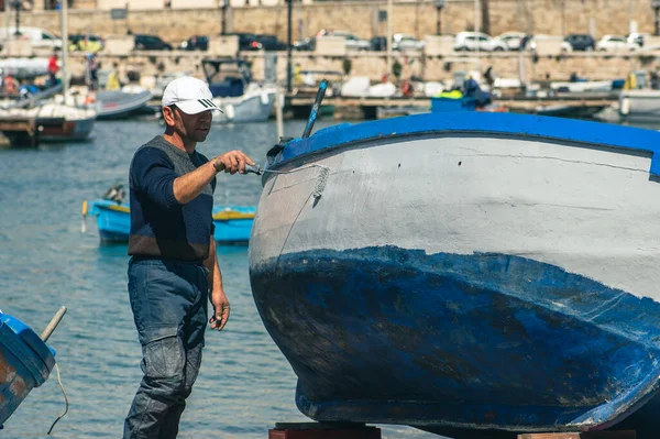 Bari, Puglia, İtalya - 8 Nisan 2023: Puglia İtalya 'nın Bari limanındaki eski bir ahşap balıkçı teknesini tamir eden ve boyayan balıkçı