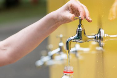 Beyaz bir kız ya da kadının plastik şişeyi şehirdeki bir çeşmeden taze suyla doldurması, sıcak hava ve yaz konsepti