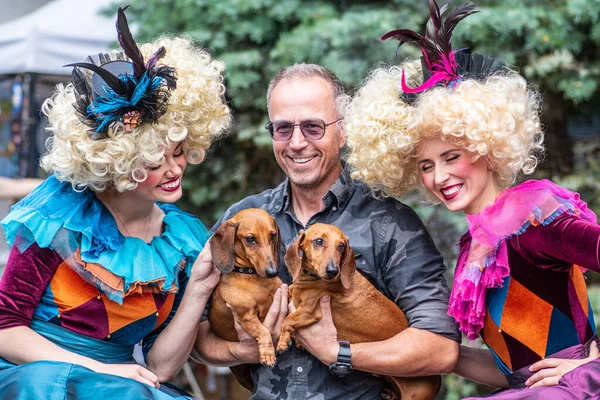 Riga, Letonya - 10 Temmuz 2023: Renkli elbise ve peruklu güzel bir çift ülke çapında Letonya Şarkı ve Dans Festivali sırasında bir adam ve iki köpeğiyle fotoğraf çekiyor 