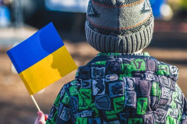 Kışlık kıyafetleri, şapkası ve Ukrayna bayrağı taşıyan çocuk ya da çocuk, çocuğun profili bayrağın üzerinde. Ukrayna 'daki savaşa Putin ve Rus saldırıları, mülteciler ve mülteci kampı neden oldu.