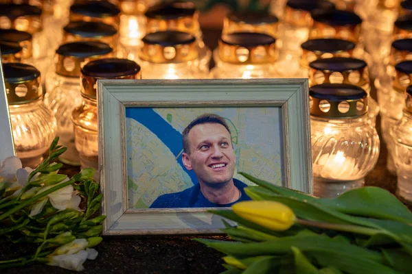 stock image Vilnius, Lithuania - February 20 2024: Flowers and candles laid at spontaneous Vilnius memorial for Russian opposition leader Alexei Navalny, with portrait wet from the snow and raindrops