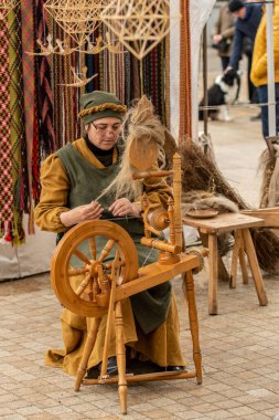 Palanga, Litvanya - 10 Mayıs 2025: Litvanya 'da bir sanat ve zanaat fuarında geleneksel giysiler içinde antik bir ahşap dokuma tezgahı üzerinde çalışan kadın 