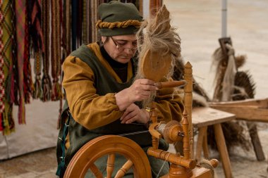 Palanga, Litvanya - 10 Mayıs 2025: Litvanya 'da bir sanat ve zanaat fuarında geleneksel giysiler içinde antik bir ahşap dokuma tezgahı üzerinde çalışan kadın 