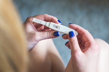 Genç sarışın kız oturuyor ve negatif hamilelik testine bakıyor.