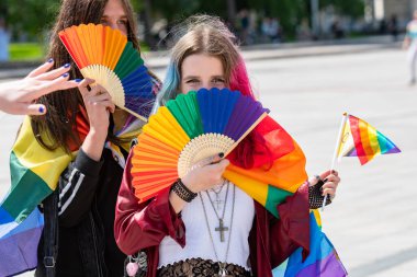 Vilnius, Litvanya - 7 Haziran 2025: Gökkuşağı renkli saçları ve yüzünü örten, LGBT + gurur yürüyüşü sırasında haç ve bayraklar takan sevimli genç kız
