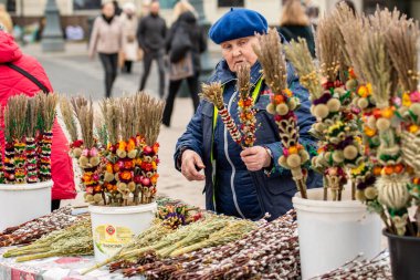 Vilnius, Litvanya - 13 Nisan 2025: Pazar günü Litvanya 'nın başkenti Vilnius' ta bulunan katedralin yakınındaki kurutulmuş çiçek ve bitkilerden yapılan geleneksel el işi süslemeler olan verbo satan yaşlı kadın