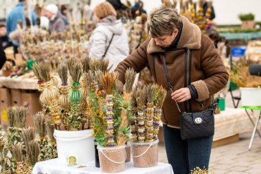 Vilnius, Litvanya - 13 Nisan 2025: Palmiye Pazar günü Litvanya 'nın Vilnius kentindeki katedralin yakınında kurutulmuş çiçek ve bitkilerden yapılan geleneksel el yapımı verbolar satın alan kadın