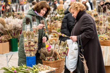 Vilnius, Litvanya - 13 Nisan 2025: Palmiye Pazar günü Litvanya 'nın Vilnius kentindeki katedralin yakınında kurutulmuş çiçek ve bitkilerden yapılan geleneksel el yapımı verbolar satan kadın