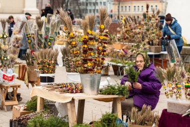 Vilnius, Litvanya - 13 Nisan 2025: Pazar günü Litvanya 'nın başkenti Vilnius' ta bulunan katedralin yakınındaki kurutulmuş çiçek ve bitkilerden yapılan geleneksel el işi süslemeler olan verbo satan yaşlı kadın
