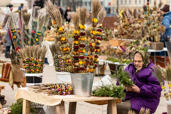 Vilnius, Litvanya - 13 Nisan 2025: Pazar günü Litvanya 'nın başkenti Vilnius' ta bulunan katedralin yakınındaki kurutulmuş çiçek ve bitkilerden yapılan geleneksel el işi süslemeler olan verbo satan yaşlı kadın