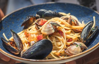 İstiridye ve siyah midyeli spagetti, taze kiraz domatesleri, maydanoz yaprakları ve mavi seramik tabakta servis edilen kara biber.