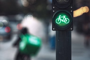 Close-up of green bicycle traffic light signal illuminated with delivery cyclist riding on urban street in background