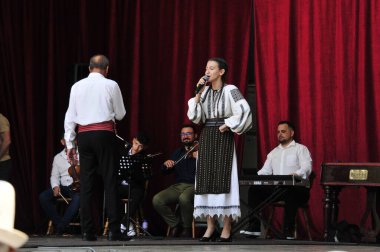 Gorj ilçesinden gelen halk müziği sanatçıları geometrik ve çiçek desenli parlak renkli geleneksel ulusal kostümler giyiyorlar..