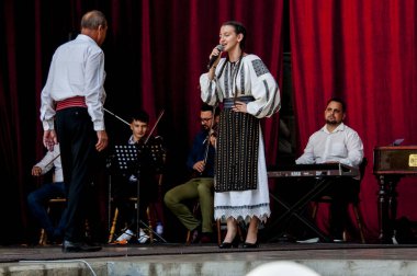 Gorj ilçesinden gelen halk müziği sanatçıları geometrik ve çiçek desenli parlak renkli geleneksel ulusal kostümler giyiyorlar..