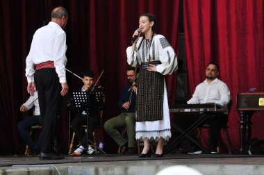 Gorj ilçesinden gelen halk müziği sanatçıları geometrik ve çiçek desenli parlak renkli geleneksel ulusal kostümler giyiyorlar..