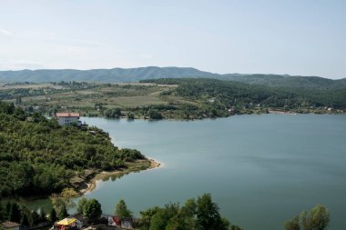 Arka planda kilise ve dağlarla gölün muhteşem manzarası.