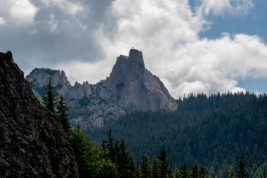 Bulutlu gökyüzünün altında yeşilliklerle çevrili güzel bir dağ manzarası