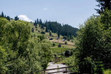 Yeşil ağaçları ve arka planda küçük bir köyü olan güzel bir dağ manzarası.
