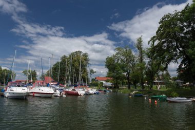 CZAPLINEK, Batı Pomeranya - POLAND - 14 Haziran 2024: Göl kenarındaki LANDSCAPE - marinaya demirlemiş bir yelkenli ve motor yatları