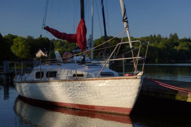 LANDSCAPE BY THE LAKE - A sailboats moored in marina in the rays of the morning sun clipart