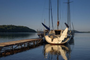 LANDSCAPE BY THE LAKE - Sailboats moored to a pier on the lake shore clipart