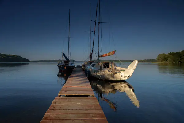 stock image STARE DRAWSKO, WEST POMERANIAN - POLAND - JUNE 25, 2024: LANDSCAPE BY THE LAKE - Sailboats moored to a pier on the lake shore