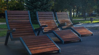 CITY PARK - Wooden loungers in the recreation area wet with morning dew clipart