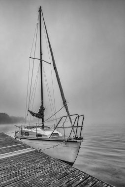 LANDSCAPE BY THE LAKE - A sailboat at the pier on a foggy day clipart