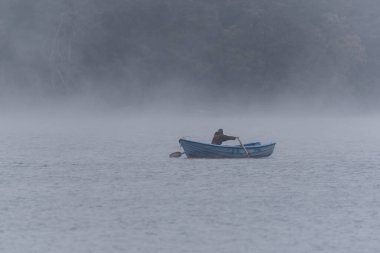 FOGGY LAKE LANDSCAPE - Angler sail by boat rowing on the lake clipart