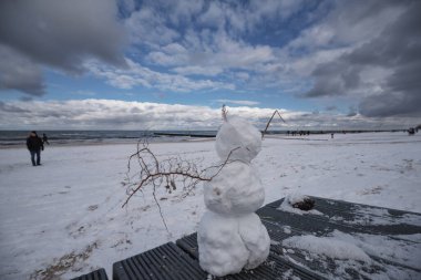 WINTER ON THE SEA COAST - Snowman and snow on the beach and people walking clipart