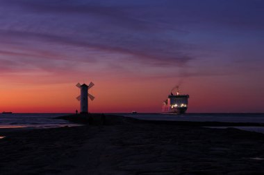 SUÇLU, Batı Pomeranya - POLAND 17 Mart 2025: Deniz kıyısında güneş doğuyor - yolcu ve feribot limana doğru yol alıyor