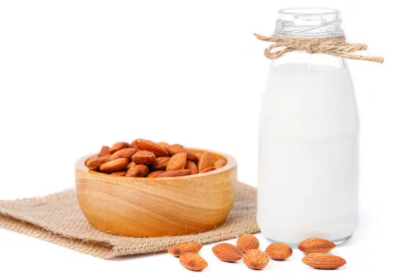 İzole edilmiş süt ve badem. Beyaz arka planda kenevir kumaş torbasında badem bulunan cam süt şişesi. Ev yapımı badem sütü. Kopyalama alanı ve kırpma yolları ile.