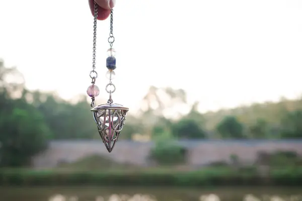 Kuvars kristal sarkacını tutmak ve kullanmak ve soru sormak için kullanmak. Kuvars Kristal Sarkaç Bir El Üzerinde Asılı