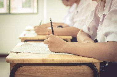 Asyalı kız öğrencilerin lise giriş sınavları için kâğıt üzerinde sınav kağıtları yazmaları. Tayland 'daki okul sınıfında üniformalı bir öğrenci. Sınav geçmişi ve eğitim konsepti, klasik ton.