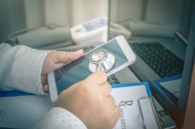 Doktor hasta notları için akıllı telefon için stetoskop kullanıyor, laptopta kan basıncı ölçümü, hastane sağlık hizmetlerinde masa ve tıbbi konsept, seçici odaklanma.