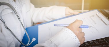 Hastane sağlık hizmetlerindeki dizüstü bilgisayara hasta notu için stetoskopla tıbbi reçeteli kağıt pano yazan doktor.