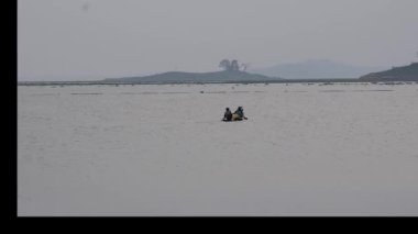 Bir balıkçı alacakaranlıkta gölde balık tutarken ahşap bir tekneye kürek çeker.