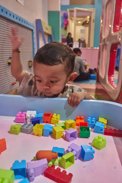 Asyalı bir çocuk renkli plastik oyuncaklarla oturup duyusal oyunlar oynuyor.