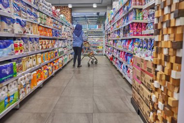 Süpermarkette tesettür takan Asyalı kadın, mağaza rafları arasında günlük ihtiyaçlarını arıyor