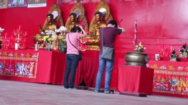 Çinli bir adam ve bir kadın tapınağın sunağında Buda heykellerinin önünde ve duvarda asılı tanrıların resimlerinin önünde dua ediyorlar..