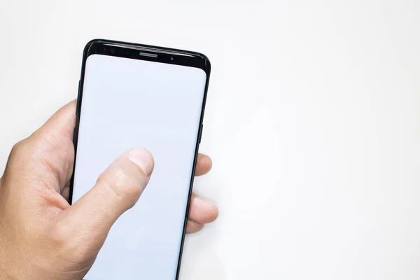 白い背景にスマートフォンを保持します 男性の手は テンプレートとして白い画面でスマートフォンをスクロールします 白い背景と空のスマートフォンフレーム 電話画面上の親指指 — ストック写真