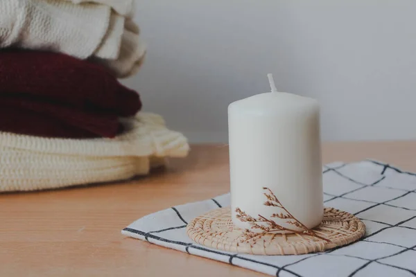 white candle with a pile of sweaters on white background, autumn, cozy  home