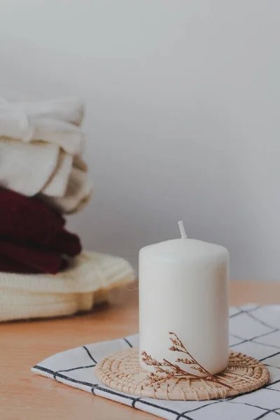 white candle with a pile of sweaters on white background, autumn, cozy  home