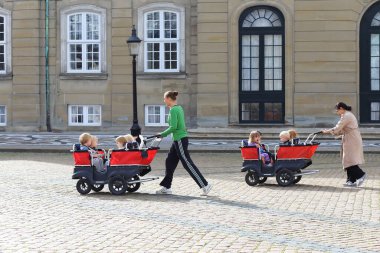 Kopenhag, Danimarka-Ağustos 17, 2023: Kraliyet sarayının yakınındaki meydanda yürüyüş yapan anaokulu. Bakıcılar bisiklet kasklı çocuklarla bebek arabalarını taşırlar. Çocuklar için günlük bakım