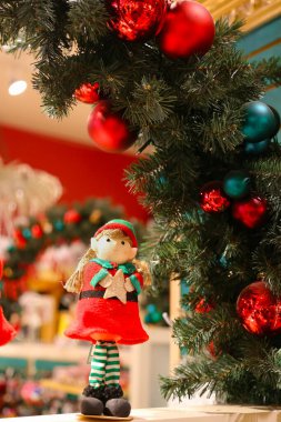 Çam kozalakları ve çay mumu ışığının yanında elinde ladin dalı tutan Noel Elf heykelciğine odaklan. Karanlık bir akşam odası ve bir sürü odağı olmayan parti ışıkları..