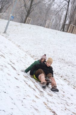 Çocuklar karlı bir parkta yürüyor, yürüyor, kızakla kayıyor ve oynuyorlar. Çocuklarla kış eğlencesi ve açık hava aktiviteleri