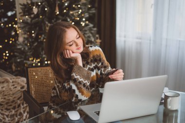 Bilgisayarda ya da internetten alışveriş yapan gülümseyen kadın portresi, arka planda süslü Noel ağacı olan yeni yıl hediyeleri almak, klavyede daktilo yazmak. Yüksek kalite fotoğraf