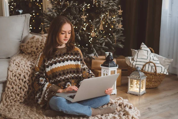 stock image Portrait of smiling woman working on laptop or shopping online, buying new year presents with decorated Christmas tree on background, typing on keyboard. High quality photo