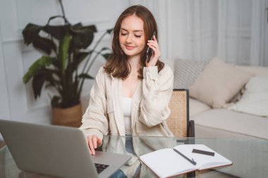 Akıllı telefondan konuşan, kalemle not alan, bilgisayarla evden uzak iş yapan, masa başında otururken bilgi yazan çok görevli kızıl saçlı serbest kadın. Uzaktan çalışan kız