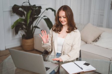 Neşeli kızıl saçlı kız bilgisayardan, ev ofisten, bilgisayardan gülüyor ve konuşuyor, uzaktan çalışıyor, stratejiyi anlatıyor, serbest çalışıyor, takımla yeni bir projeyi tartışıyor.